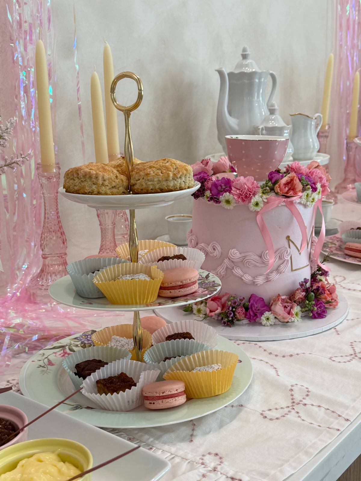 A tiered stand of scones and pastries beside a floral-crowned cake