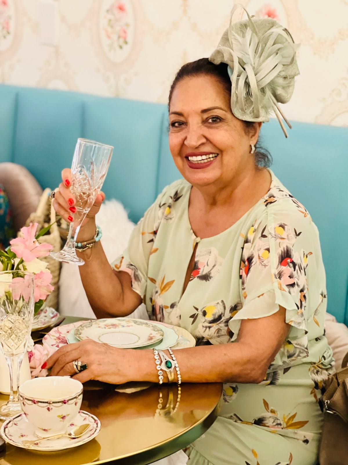 A smiling guest in a mint fascinator raising a crystal glass at afternoon tea