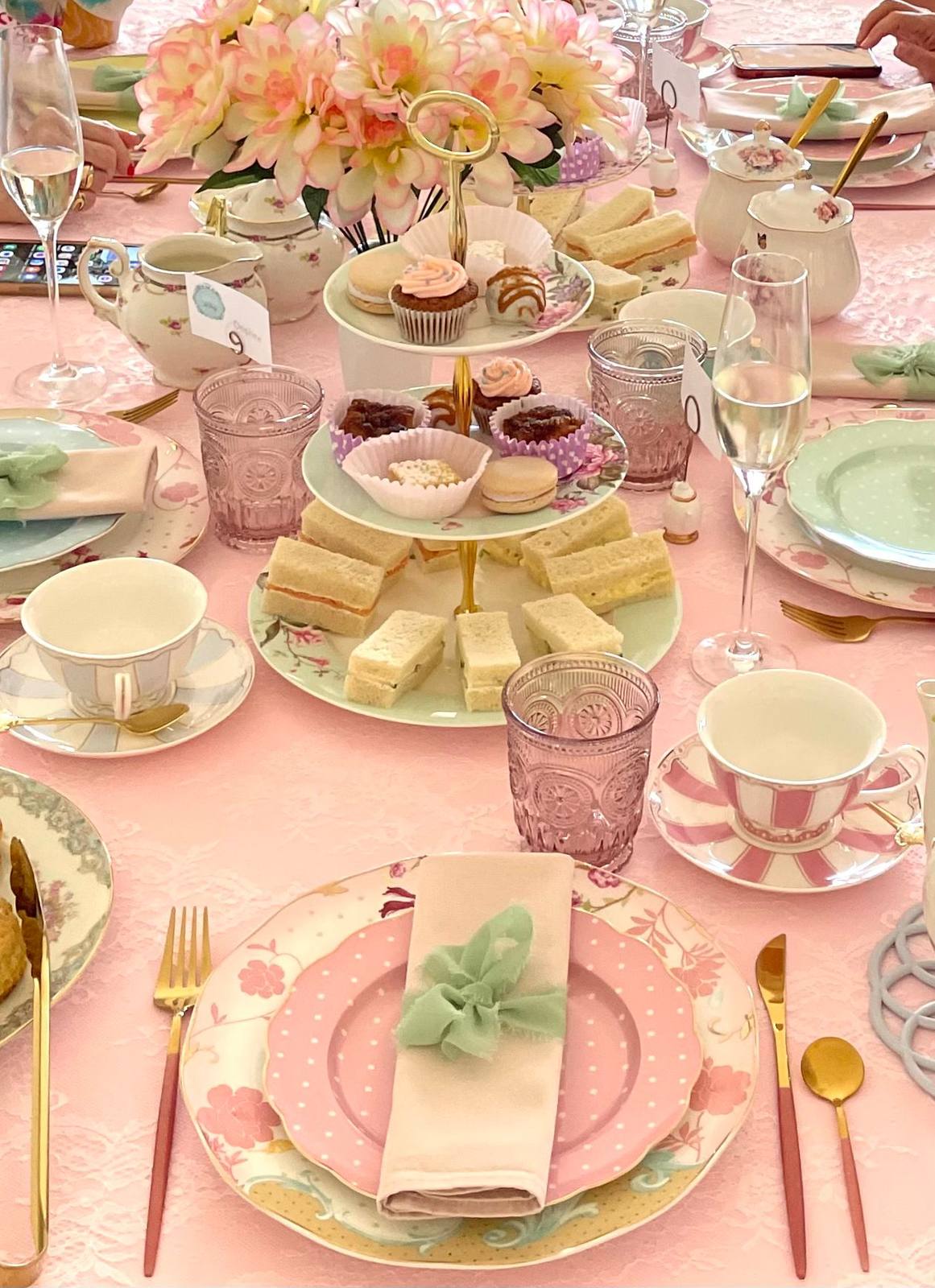 Finger sandwiches and pastries on a pink tablecloth with vintage teacups