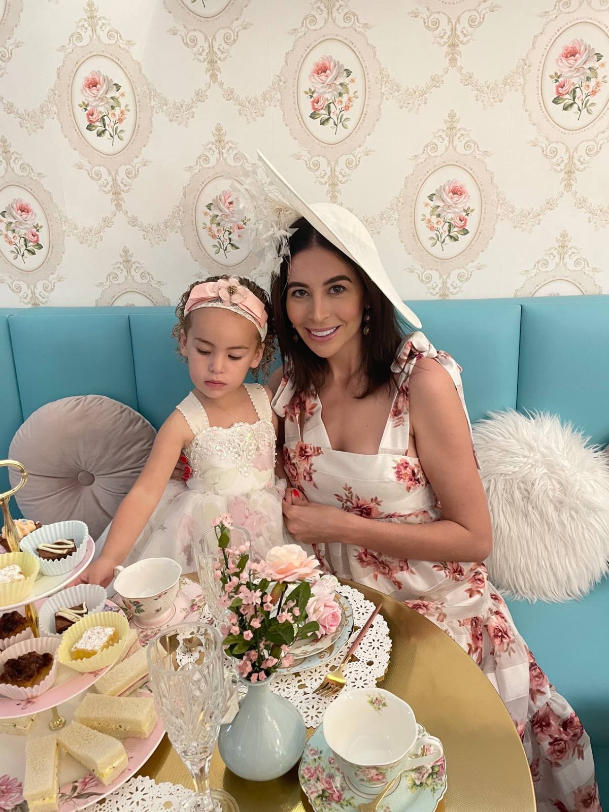 A mother and daughter in floral dresses seated at an afternoon tea table