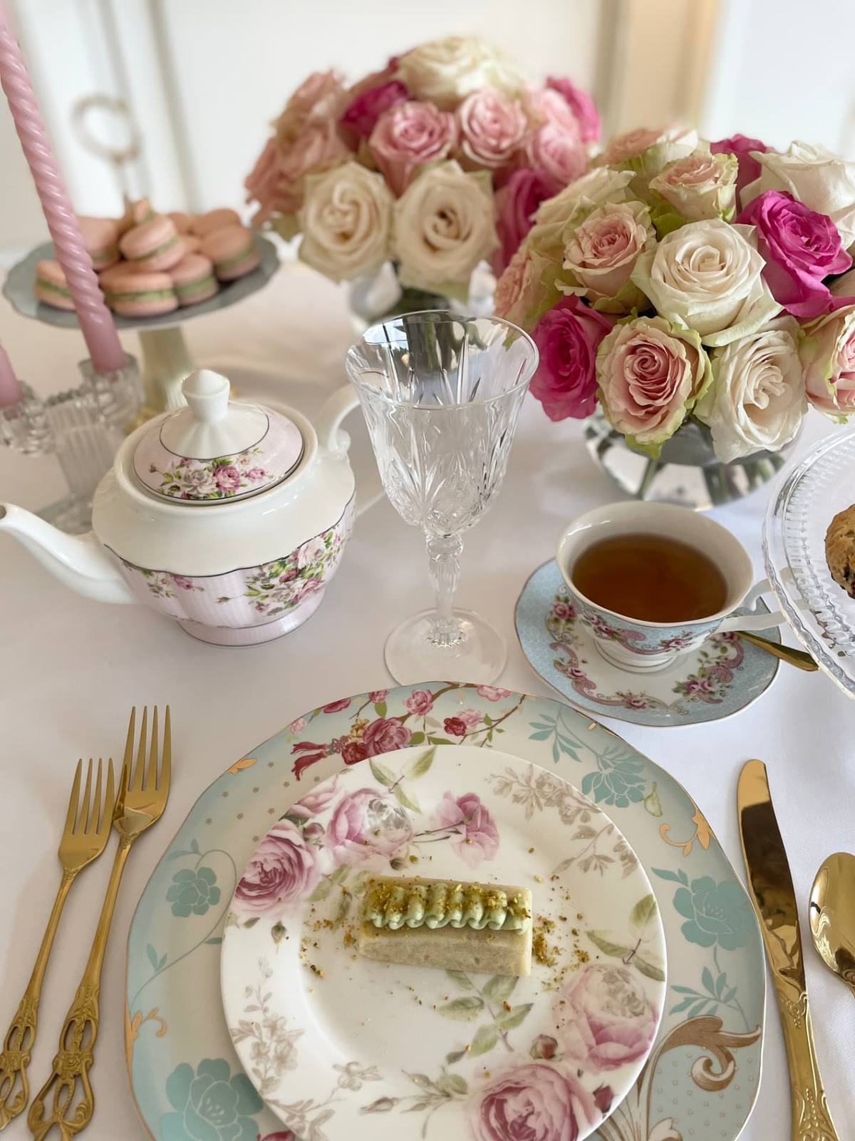 A floral teapot and teacup with gold cutlery on a lace tablecloth