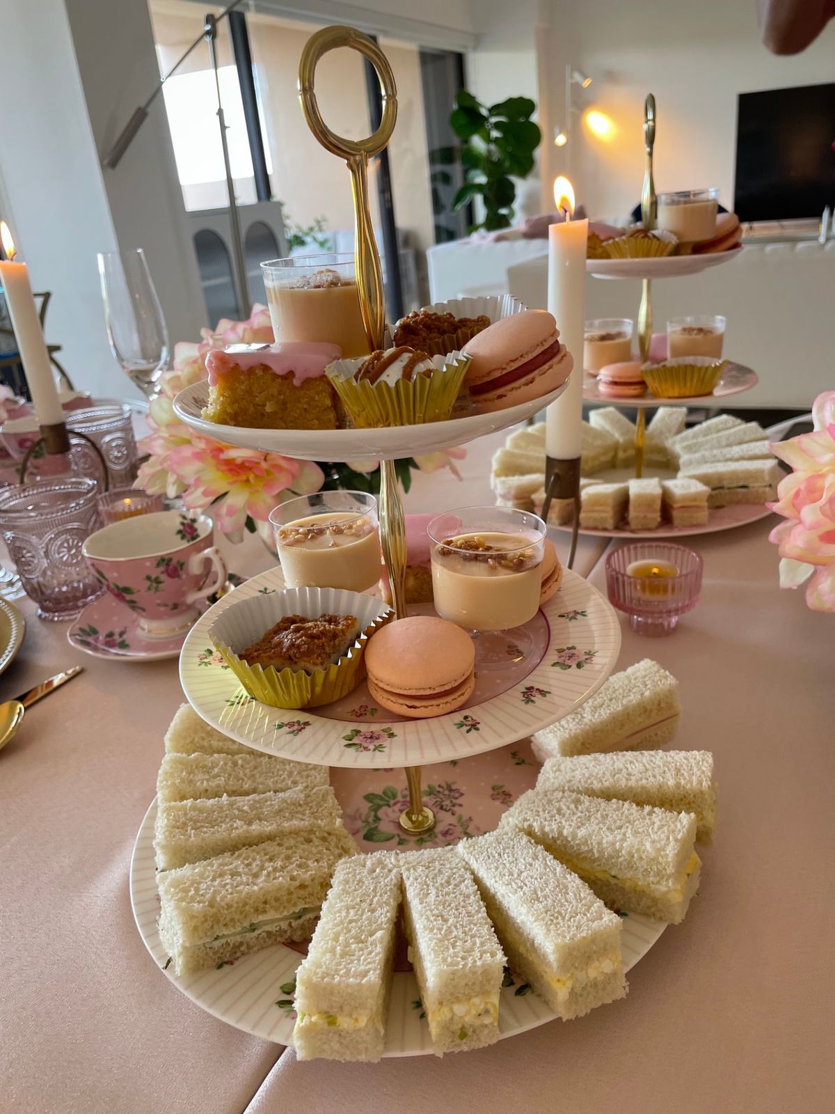 A tiered stand with macarons and sandwiches beside candlelight