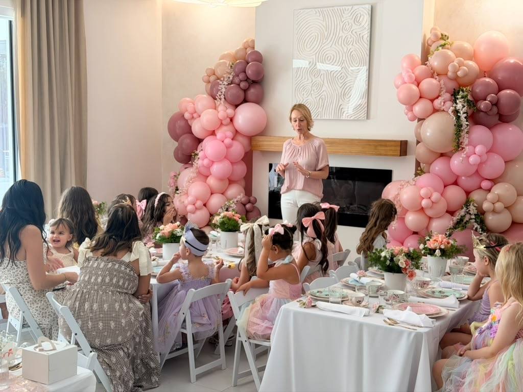 Guests seated at a pink balloon-decorated afternoon tea celebration