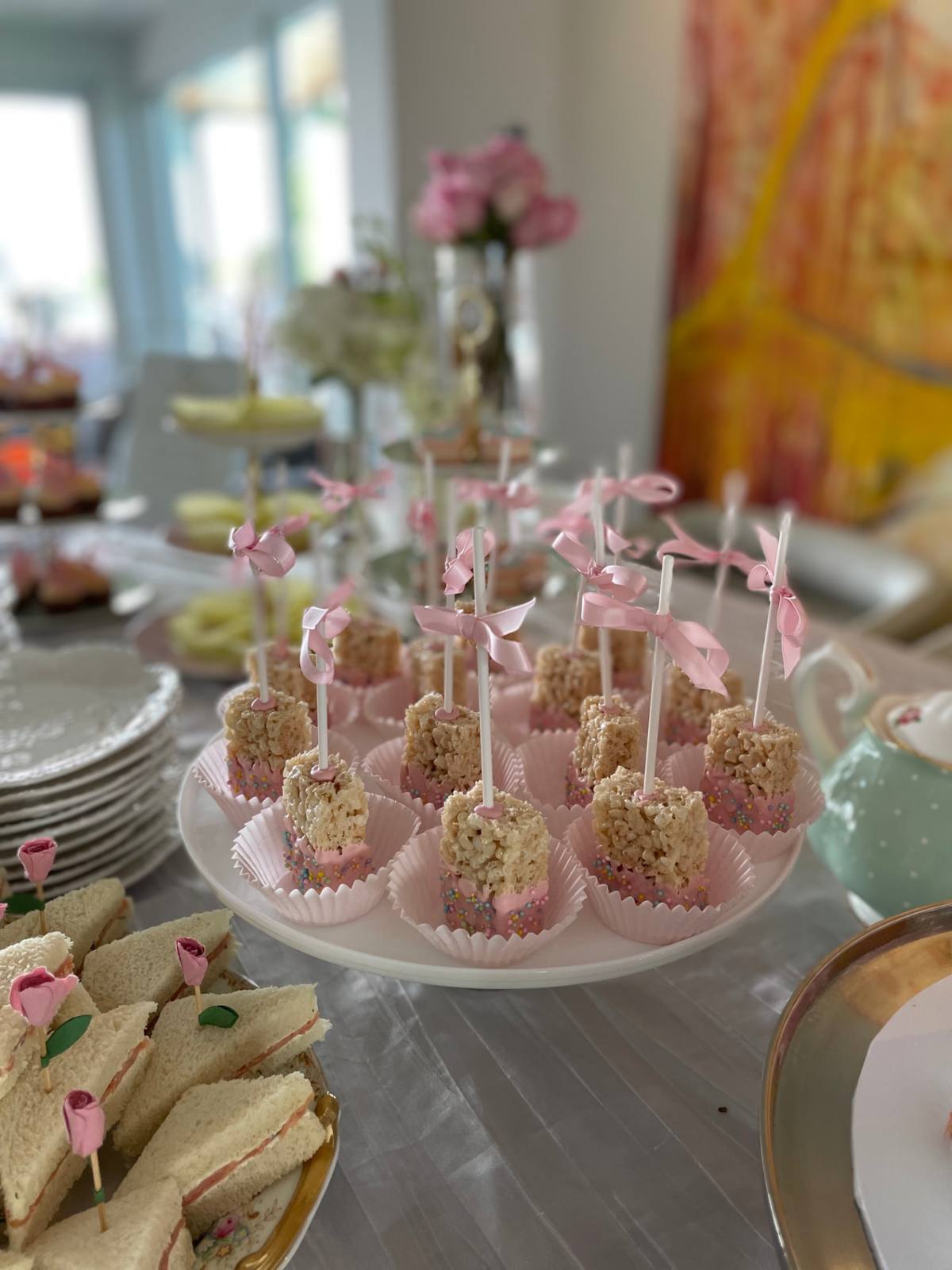 Pink-dipped treat pops tied with satin bows beside finger sandwiches