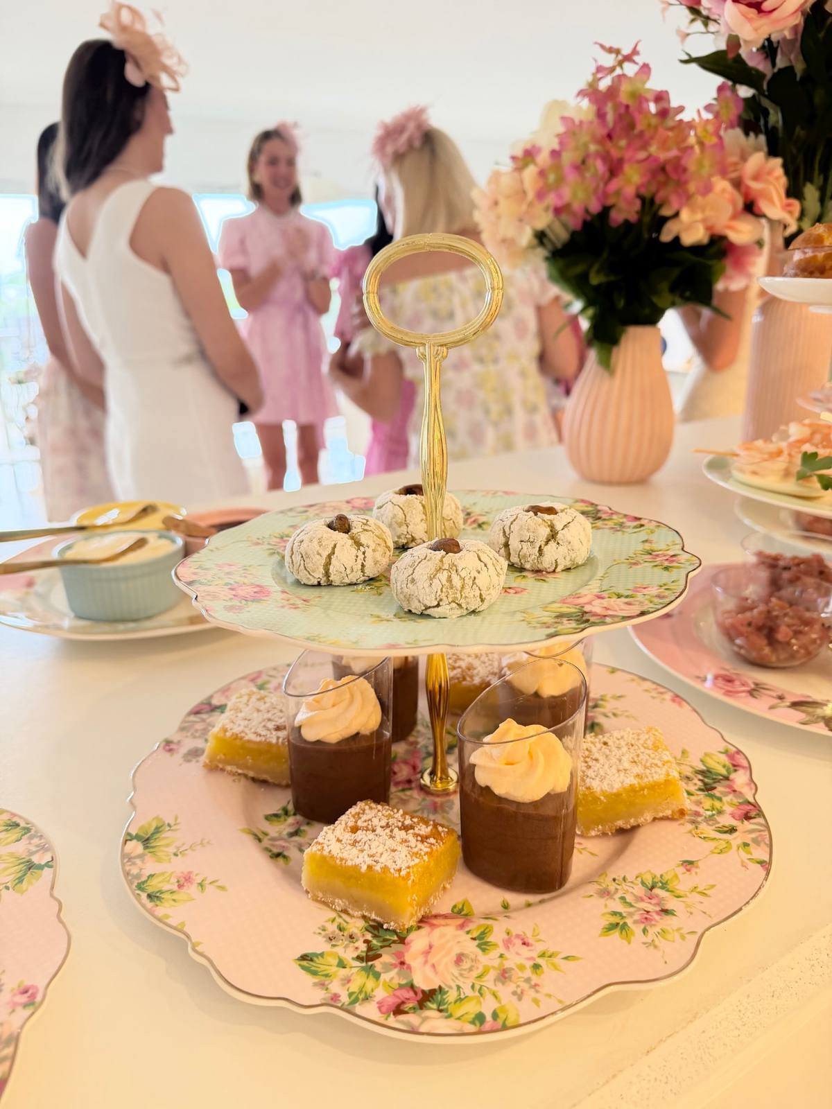 A tiered stand of mini cakes and pastries on a floral table