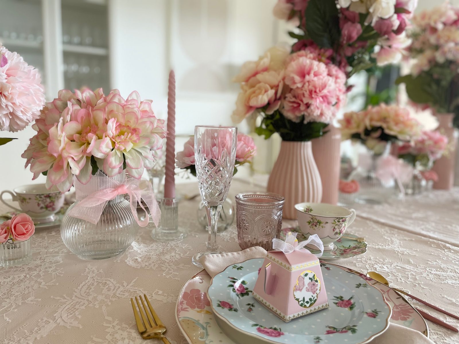 A pink paper teapot favour box on floral china with pink blooms and lace