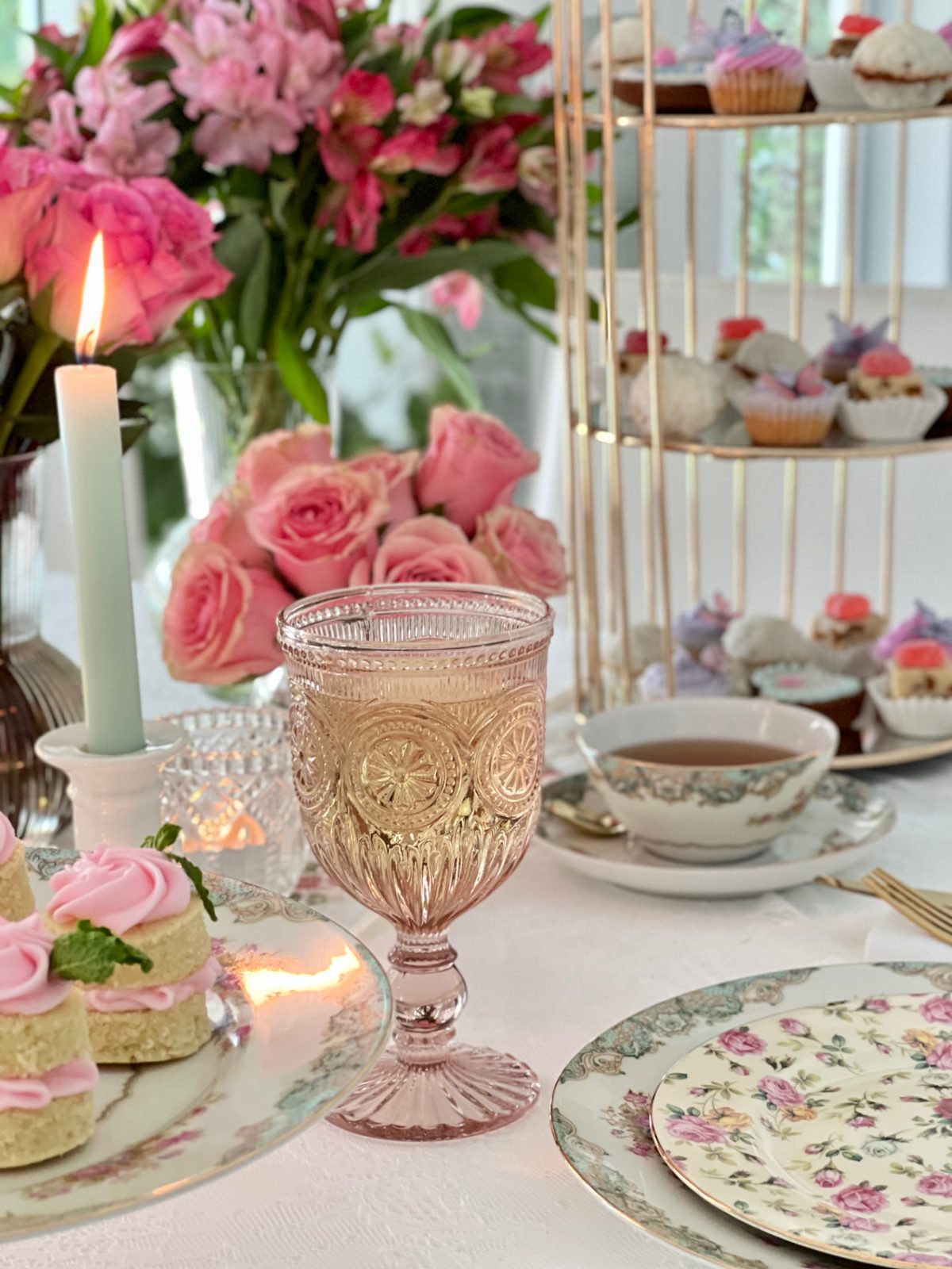 Pink pressed-glass goblet with roses, candles and a tiered stand of petits fours