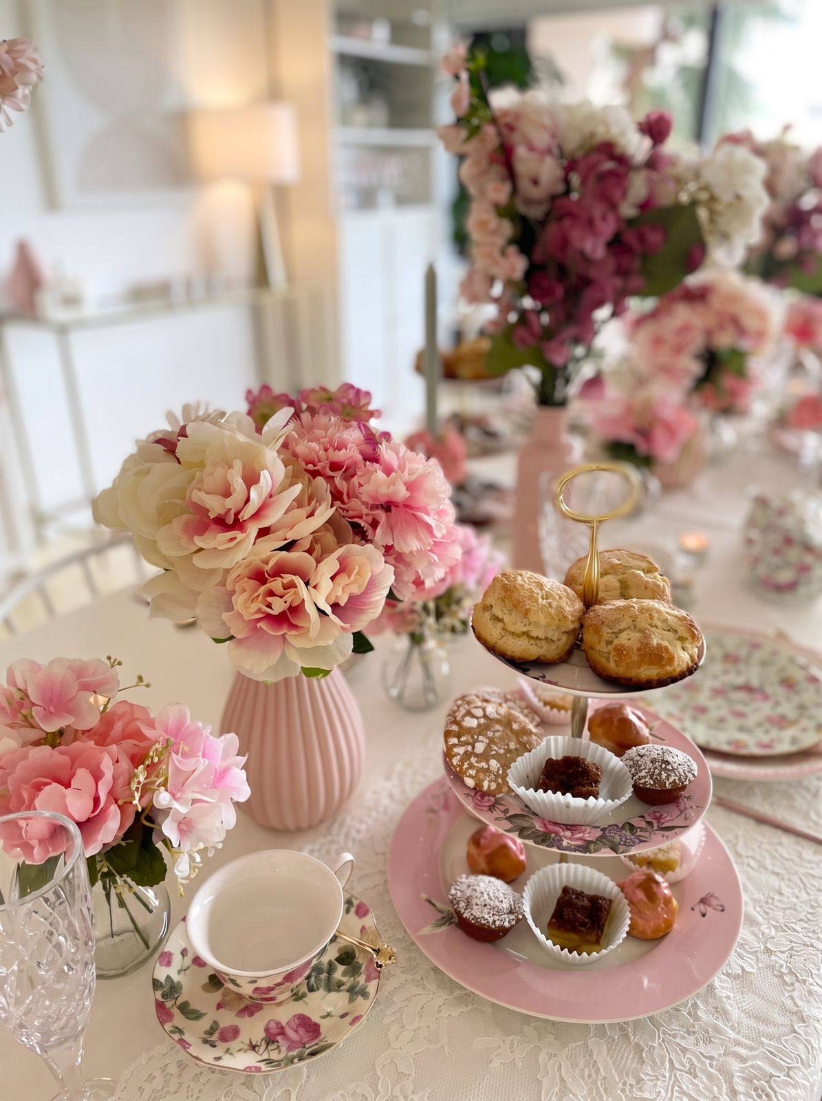 A styled afternoon tea table with a tiered stand of scones and pastries, pink florals and rose china